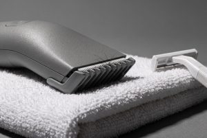 An electric body trimmer with a comb guard rests on a folded white towel, a disposable razor pushed aside