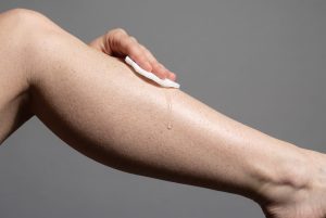 A hand swipes a soaked cotton pad down a fair, freckled shin as a clear drop runs over the skin