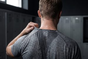 A man in a locker room pulls a sweat-soaked training shirt away from his neck after a workout