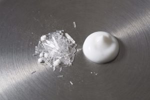 Clear needle-shaped urea crystals beside a dab of white cream on brushed steel