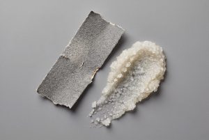A torn strip of coarse sandpaper beside a smear of salt body scrub with similarly sharp grains